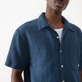Model wearing Farah Vintage Olsen Textured Shirt in Aegean Blue, short sleeves, pointed collar, white tee visible underneath