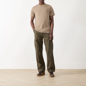 Model wearing Farah Vintage Danny Logo T-Shirt in Stone Grey with olive cargo trousers and brown trainers.