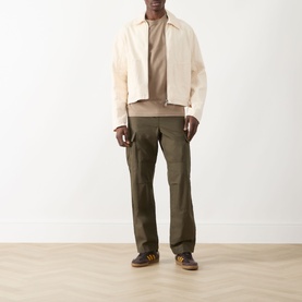 Model wearing Farah Vintage Danny Logo T-Shirt in Stone Grey, styled with cream jacket, olive cargo trousers and navy trainers.