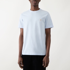 Model wearing pale blue crew neck t-shirt with small gold logo embroidery on chest, short sleeves, relaxed fit