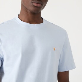 Model wearing pale blue crew neck T-shirt with small gold Farah logo embroidery on chest, short sleeves, close-up shot