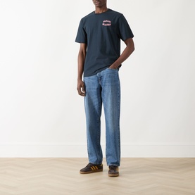 Model wearing Farah Vintage Caligo Logo T-Shirt in True Navy with light-wash straight-leg jeans and brown suede trainers.