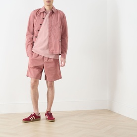 Model wearing Farah Vintage Stacy Logo Pocket T-Shirt in Dusty Red, styled with matching pink overshirt, shorts, and red trainers.
