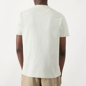 Model wearing Farah Vintage Danny Logo T-Shirt in Soft Green, rear view, crew neck, short sleeves, styled with beige trousers.