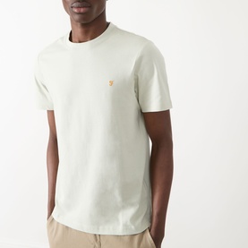 Model wearing Farah Vintage Danny Logo T-Shirt in Soft Green, crew neck, short sleeves, small chest logo, styled with beige trousers.