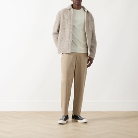 Model wearing Farah Vintage Danny Logo T-Shirt in Soft Green, styled with a beige borg jacket, taupe trousers and black canvas high-top trainers.