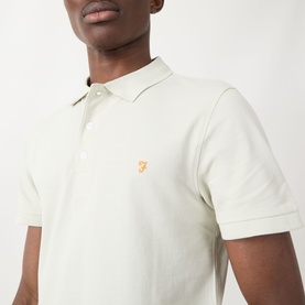 Model wearing Farah Vintage Blanes Logo Polo Shirt in Soft Green, showing polo collar, short sleeves and orange embroidered logo detail.