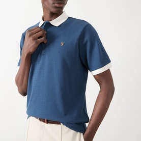Model wearing Farah Vintage Clement Logo Contrast Collar Polo Shirt in Aegean Blue with white contrast collar and cuffs, styled with cream trousers.