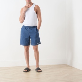 Model wearing Farah Vintage Edgar Logo Textured Swim Shorts in Soft Green with contrast stitching, styled with a white vest and dark sandals