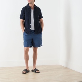 Model wearing Farah Vintage Edgar Logo Textured Swim Shorts in Soft Green, styled with a navy short-sleeve shirt, white tee, and dark slides.