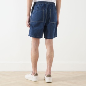 Model wearing Farah Vintage Swinton Logo Drawstring Shorts in Aegean Blue denim with white trainers, rear view showing back pockets.