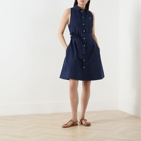 Model wearing Polo Ralph Lauren Polo Player Mini Shirt Dress in navy, sleeveless with self-tie belt and button front, styled with tan flat sandals.