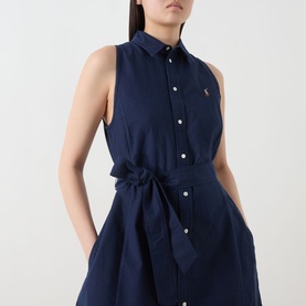 Model wearing Polo Ralph Lauren Polo Player Mini Shirt Dress in navy, sleeveless with pointed collar, self-tie belt and button fastening