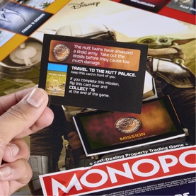 Star Wars: The Mandalorian and Grogu Monopoly game card held above board, showing Mission card with Hutt Twins artwork and Monopoly logo visible