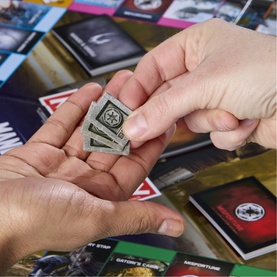 Star Wars: The Mandalorian and Grogu Monopoly metal token being passed between two hands, with game cards spread in the background