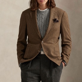 Model wearing brown textured wool blazer with notch lapels and pocket square, styled with grey cable-knit jumper and charcoal trousers