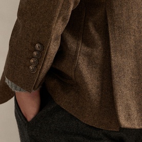 Close-up of brown herringbone blazer sleeve showing three-button cuff detail, styled with grey trousers