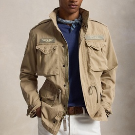 Model wearing khaki military-style jacket with multiple chest pockets, styled with navy top and blue bandana