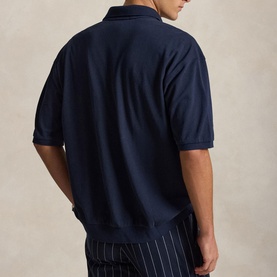 Model wearing navy blue polo shirt, back view, paired with white pinstripe trousers