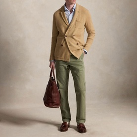 Model wearing Ralph Lauren sage green chinos with a tan double-breasted knit blazer and brown loafers, carrying a brown leather holdall.