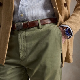 Model wearing Ralph Lauren sage green men's chinos with brown leather belt, styled with camel blazer and blue watch.