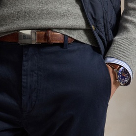 Model wearing navy chinos with a tan brown leather belt with silver buckle, styled with a grey knit sweater and blue watch