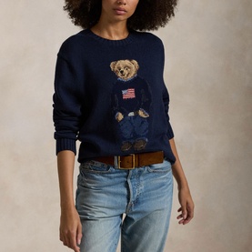 Model wearing navy knit sweater with Polo Bear American flag graphic, styled with light wash jeans and tan leather belt