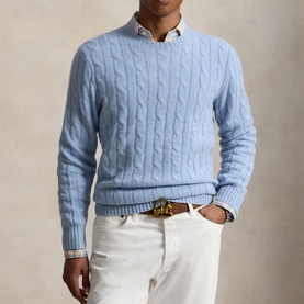 Model wearing light blue cable-knit crew neck sweater, styled with white chinos and a brown leather belt.