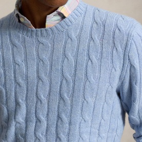 Model wearing a pale blue cable-knit crew neck sweater, styled with a pastel check shirt visible at the collar.