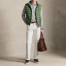 Model wearing Ralph Lauren green quilted gilet over grey polo, styled with white trousers, brown belt, and carrying a brown tote bag.