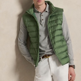 Model wearing Ralph Lauren green quilted hooded gilet, styled with grey polo shirt, white trousers and brown belt