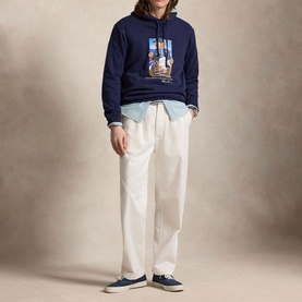 Model wearing Ralph Lauren navy graphic hoodie with white trousers, light blue shirt, and navy trainers.