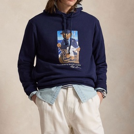 Model wearing Ralph Lauren navy hoodie with Polo Bear graphic print, styled with light wash denim jacket and cream trousers