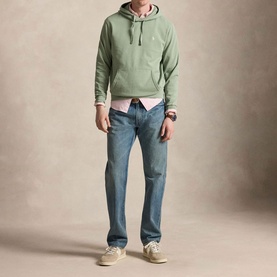 Model wearing Ralph Lauren light green hoodie, styled with a pink shirt, mid-wash blue jeans, and cream trainers.