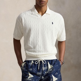 Model wearing Ralph Lauren white cable-knit polo shirt with open collar and navy pony logo, styled with navy printed swim shorts