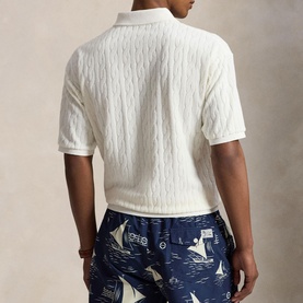 Model wearing Ralph Lauren white cable-knit polo shirt, short sleeves, paired with navy nautical-print shorts, rear view.