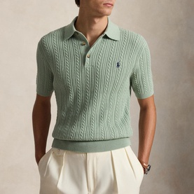Model wearing sage green cable-knit short-sleeve polo shirt with contrast logo, styled with cream tailored trousers
