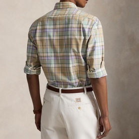 Model wearing Ralph Lauren Reg Shirt in khaki and faded mint plaid, with white trousers and brown belt, sleeves rolled up, rear view.