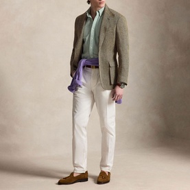 Model wearing a brown tweed blazer, mint shirt, white trousers, and tan suede loafers, with a purple scarf accessory.