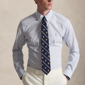 Model wearing Ralph Lauren Reg Shirt in Cabana Blue and White check, styled with a navy emblem-print tie and cream trousers.