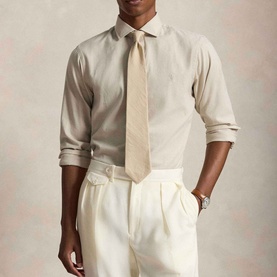 Model wearing Ralph Lauren Performance Twill Logo Shirt in Expedition Dune Heather, styled with a cream tie and white trousers.