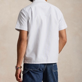 Model wearing Ralph Lauren Reg Shirt in white and royal blue stripe, short sleeves, styled with dark wash jeans, rear view.