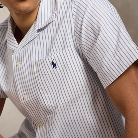 Model wearing Ralph Lauren Reg Shirt in white with navy pinstripes, short sleeves, camp collar, chest pocket, and embroidered polo pony logo.