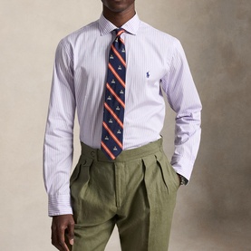Model wearing Ralph Lauren powder purple and white striped reg shirt, styled with a navy motif tie and olive pleated trousers.