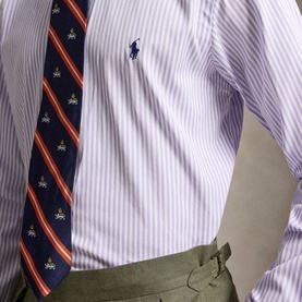 Model wearing Ralph Lauren Reg Shirt in powder purple and white stripe, styled with a navy striped tie and olive trousers.