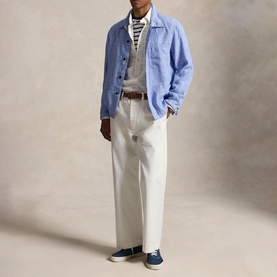 Model wearing light blue overshirt, layered over grey knit and striped top, styled with cream wide-leg trousers and navy canvas trainers