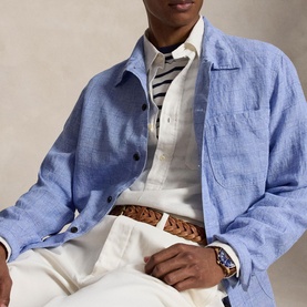 Model wearing blue linen overshirt, styled with striped shirt, white trousers and woven leather belt