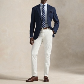 Model wearing Ralph Lauren light blue single cuff regular shirt with navy blazer, striped tie, and white trousers.