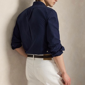 Model wearing Ralph Lauren navy slim shirt with gold Polo Pony, styled with white trousers and brown leather belt. Back view.