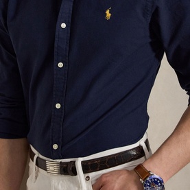 Model wearing Ralph Lauren navy slim shirt with yellow polo pony logo, styled with cream chinos and brown leather belt.